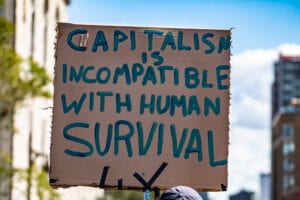 A close up shot of a cardboard sign saying capitalism is incompatible with human survival, as environmental activists stage a rally on a city street
