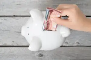 A boy's hand inserting a fifty-dollar banknote into a piggy bank.