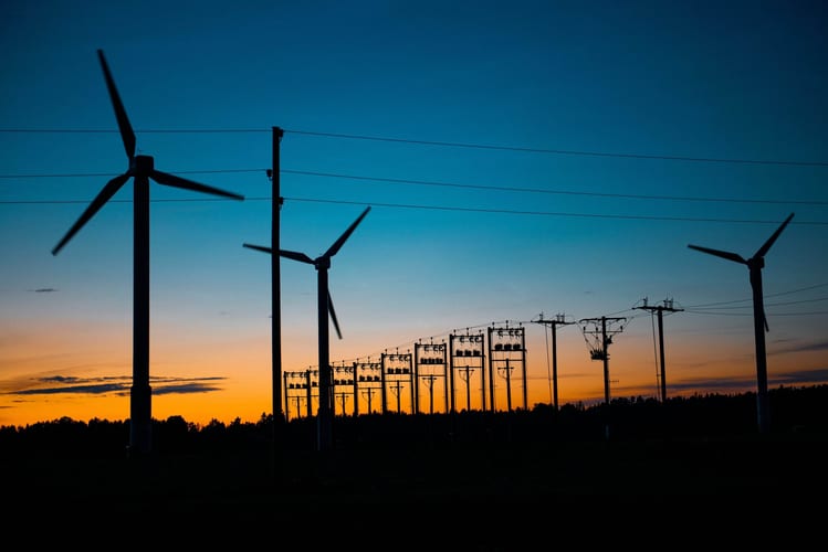 Energy lines and wind turbines with a sunset in the background.